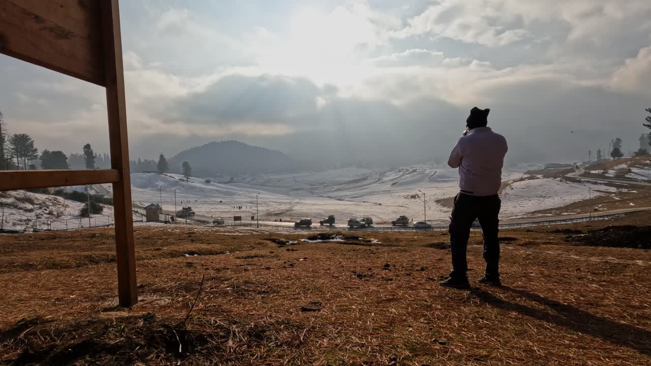 person taking a photography of snow mountain with sun rays, sky and clouds at day time, pan shot, 4k.