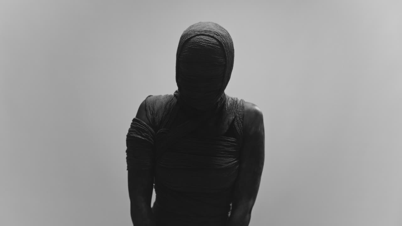 A mummy of a woman on a white backdrop moves her head