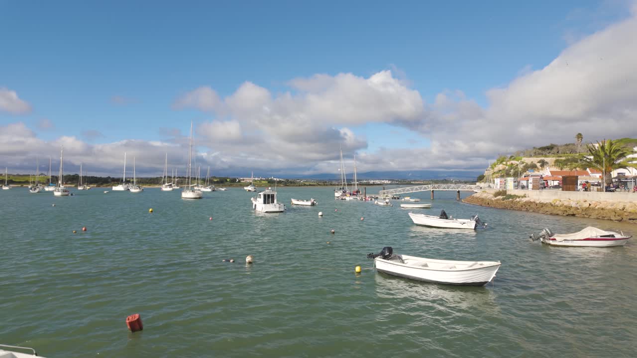 White boats floating on the water near the beach in Alvor, Portugal, with restaurants and palm trees on the shore