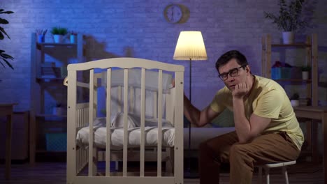 a tired young father falls asleep and a newborn in baby bed at night