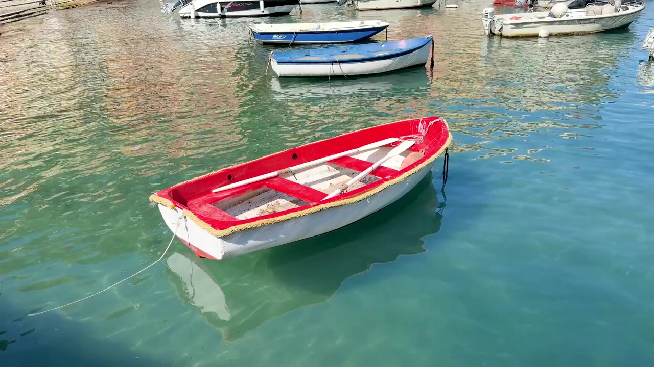 Piccola barca a remi rossa e bianca che galleggia in un porto mediterraneo soleggiato