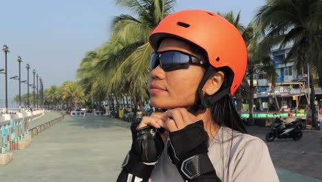 female inline skater puts on protective helmet, preparing to skate at the park in thailand