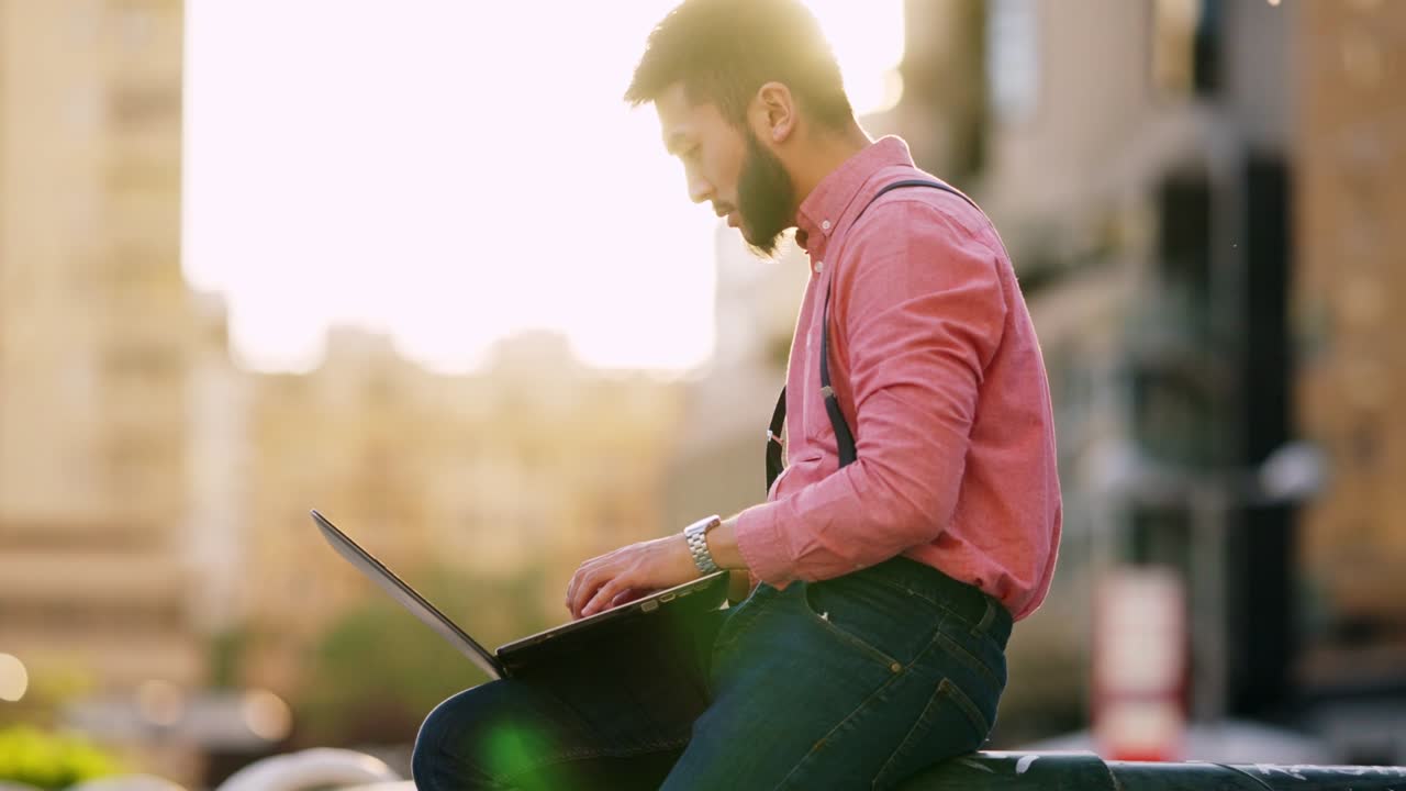 Asian man working with a laptop outside with a urban landscape in the background