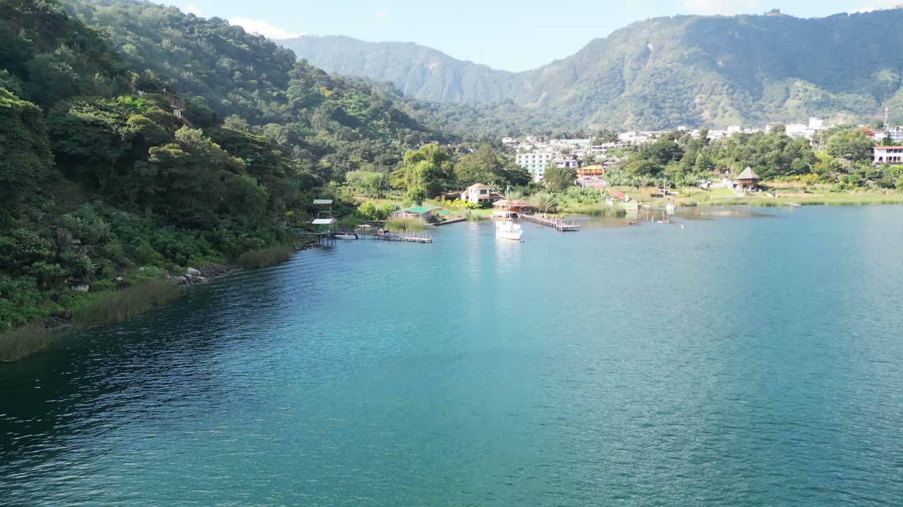 vista de avión no tripulado en guatemala volando sobre un lago azul rodeado de montañas verdes y volcanes en un día soleado en aitlan