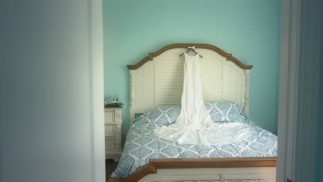 A-bridal-gown-displayed-on-a-bed-in-a-blue-bedroom-as-seen-through-a-doorway
