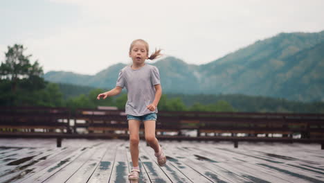 blonde child runs playing on wooden board deck after rain