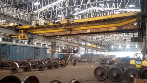 interior of a large industrial warehouse or factory specifically a railway workshop. large yellow overhead crane system suspended from the ceiling, used for lifting and moving heavy objects