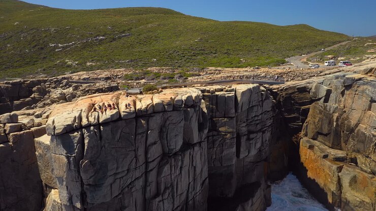 Ripresa aerea che mostra delle ragazze in cima al punto panoramico The Gap, sulla costa dell'area di Sydney, in una giornata di sole, in Australia - inquadratura da drone con tracking, ascesa e inclinazione.