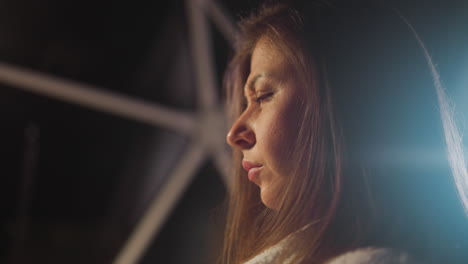 young woman with brunette hair immersed in thoughts sits alone in semi-dark living room. thoughtful female looks away and contemplates serious problems