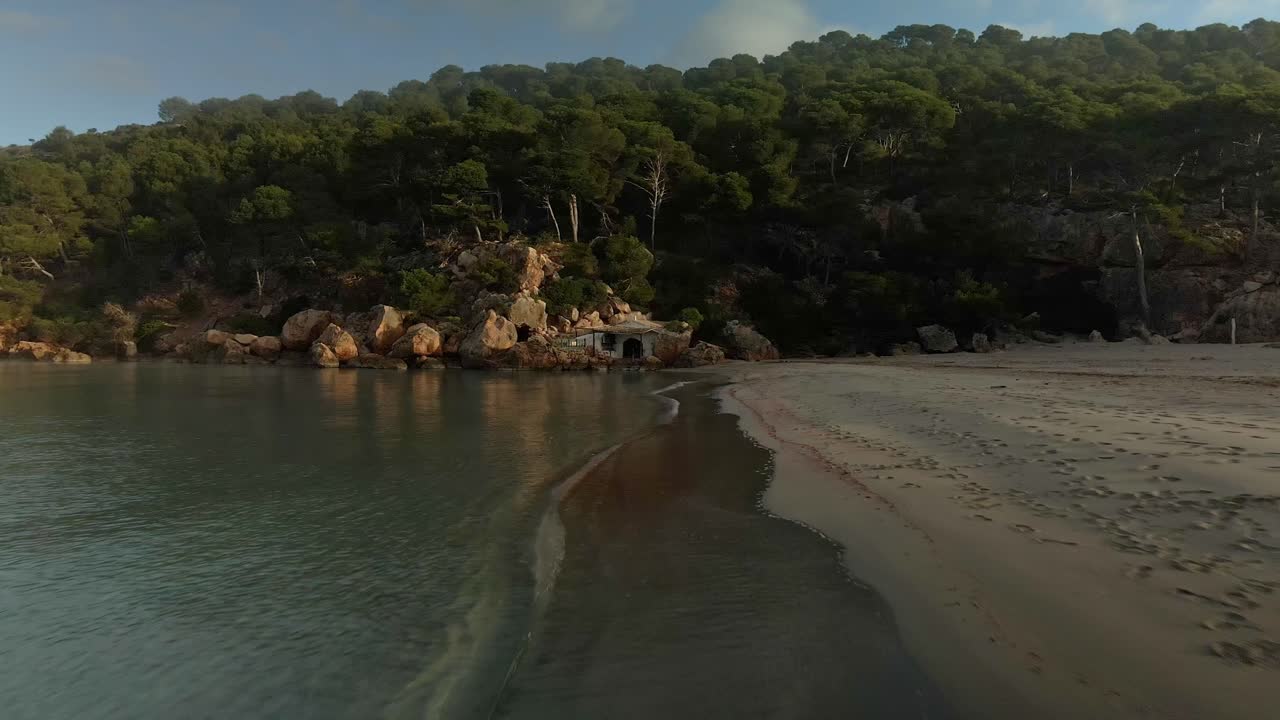 Volo di drone lungo la spiaggia con onde calme che si infrangono contro gli scogli