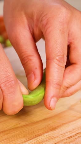 manos descascarando guisantes en una tabla de cortar de madera