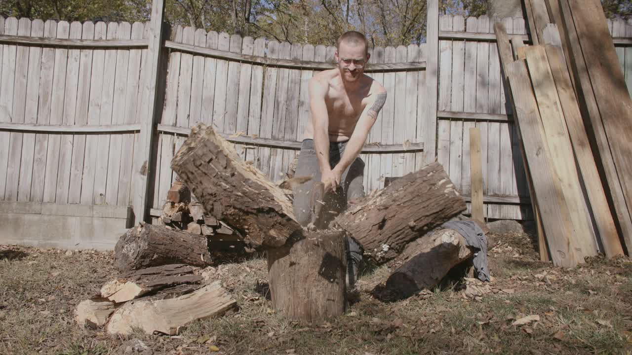 Slow motion front on wide angle of man without shirt on splitting a large log with a axe and looking satisfied