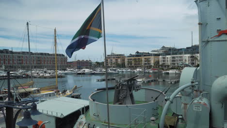 Vista-Sobre-El-Puerto-Deportivo-En-Va-Waterfront-En-Ciudad-Del-Cabo,-Bandera-Sudafricana-Ondeando-En-Primer-Plano