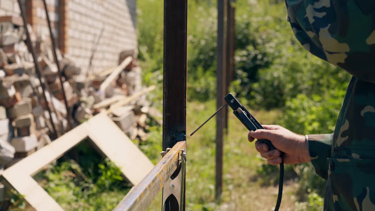 сварщик исправляет забор против кирпичной кучи и дикой травы