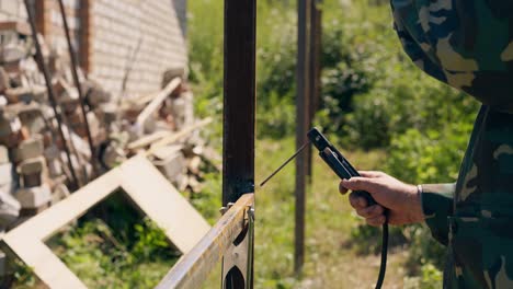 welder fixes fence against bricks pile and wild grass