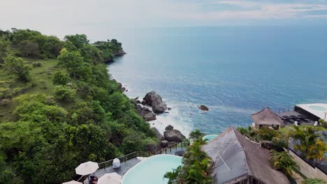 aerial drone footage captures a stunning tropical resort in bali perched on a cliffside surrounded by lush nature and endless ocean views offering a peaceful and luxurious island retreat experience.