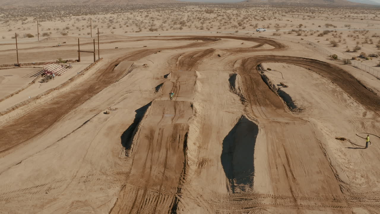 라이더가 카메라를 향해 경주할 때 사막 모터크로스 서킷 위로 뒤로 비행