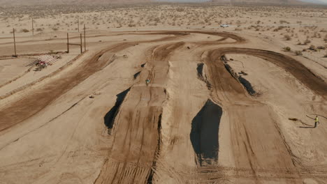 Volando-Hacia-Atrás-Sobre-El-Circuito-De-Motocross-Del-Desierto-Mientras-El-Piloto-Corre-Hacia-La-Cámara