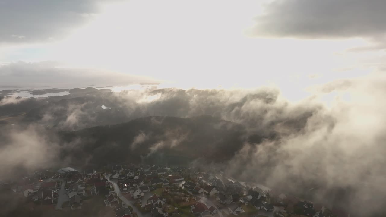imágenes de drones de una urbanización en noruega con algo de niebla flotando en el aire y el sol iluminando las nubes