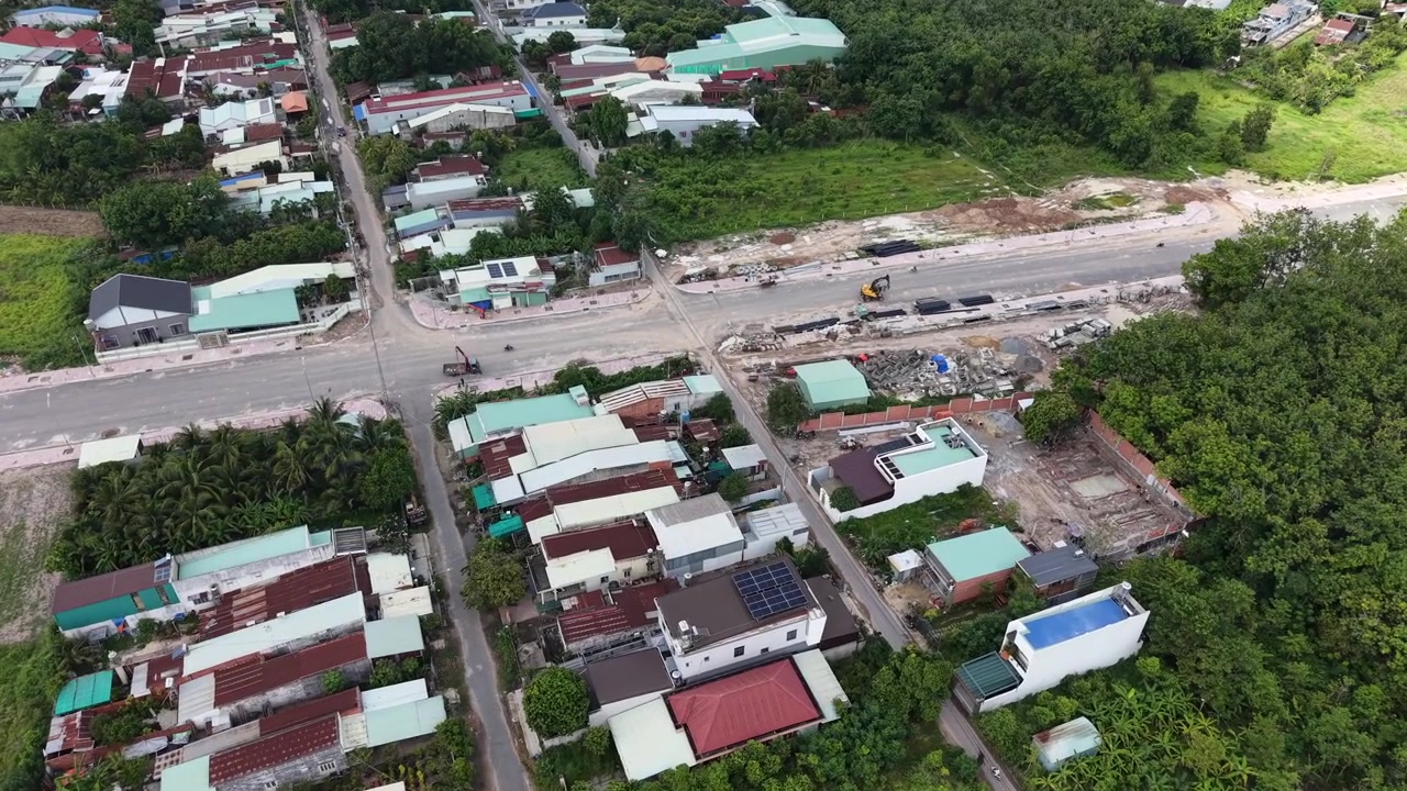 Máy bay không người lái hạ xuống và nghiêng dần từ góc nhìn rộng của một thị trấn Tây Ninh, đến khung hình từ trên cao của công trình mở rộng đường, máy xúc và các đoạn cống thoát nước xếp chồng bên dưới, Việt Nam.