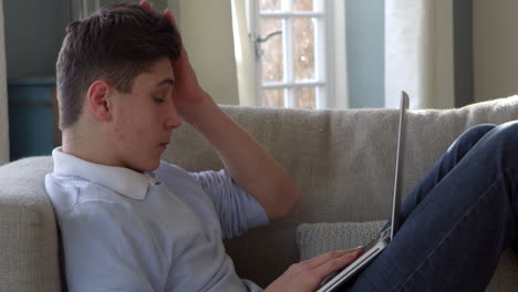 Teenage-Boy-Sitting-On-Sofa-Using-Laptop-At-Home-Shot-On-R3D