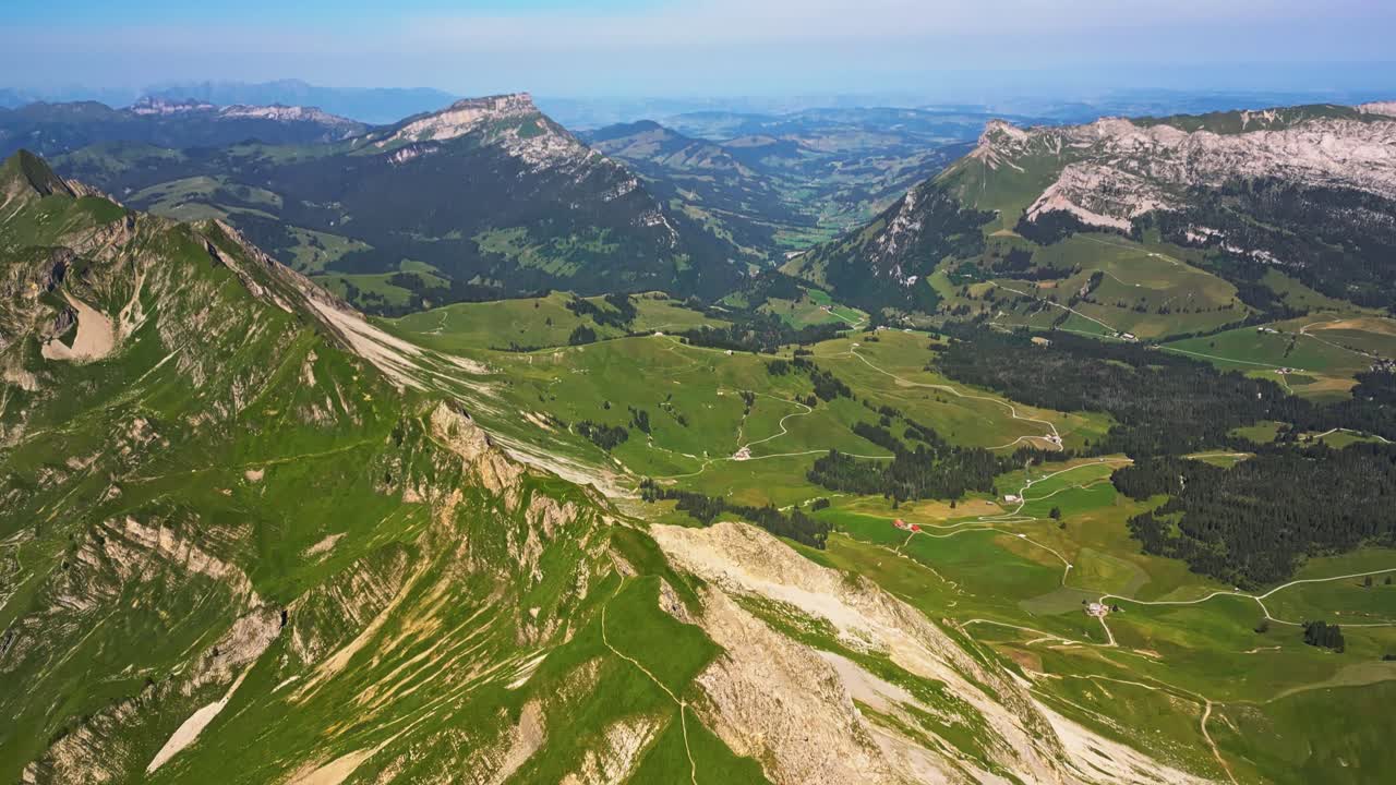 vista aérea de una vasta cordillera y un cielo azul, que panorámicas hacia abajo para revelar un alto pico que se inclina hacia abajo en un valle