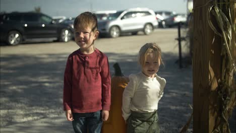 Happy-little-boy-and-girl,-brother-and-sister-smiling-at-halloween-pumpkin-patch-in-slow-motion