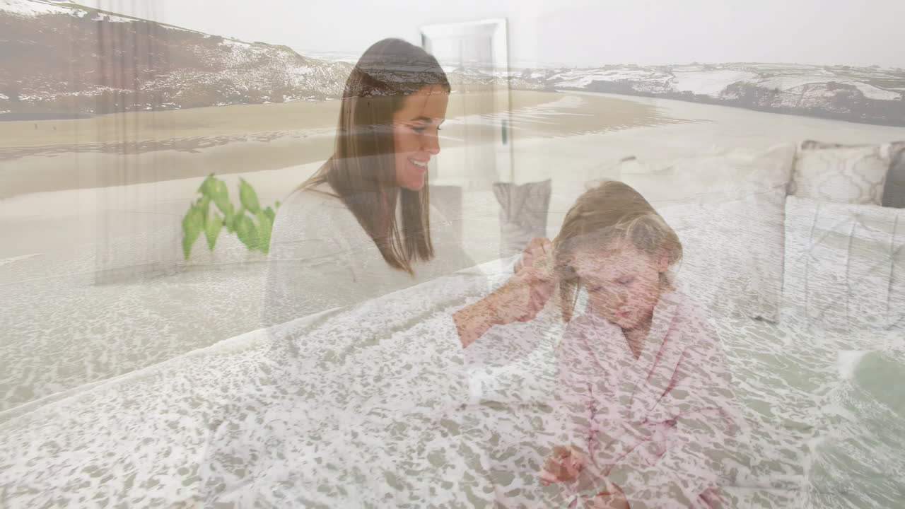 Brushing child's hair, woman on serene beach with ocean waves in background