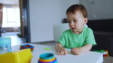 active healthy caucasian baby playing at home sitting at the desk. kid holds the toys and screams.