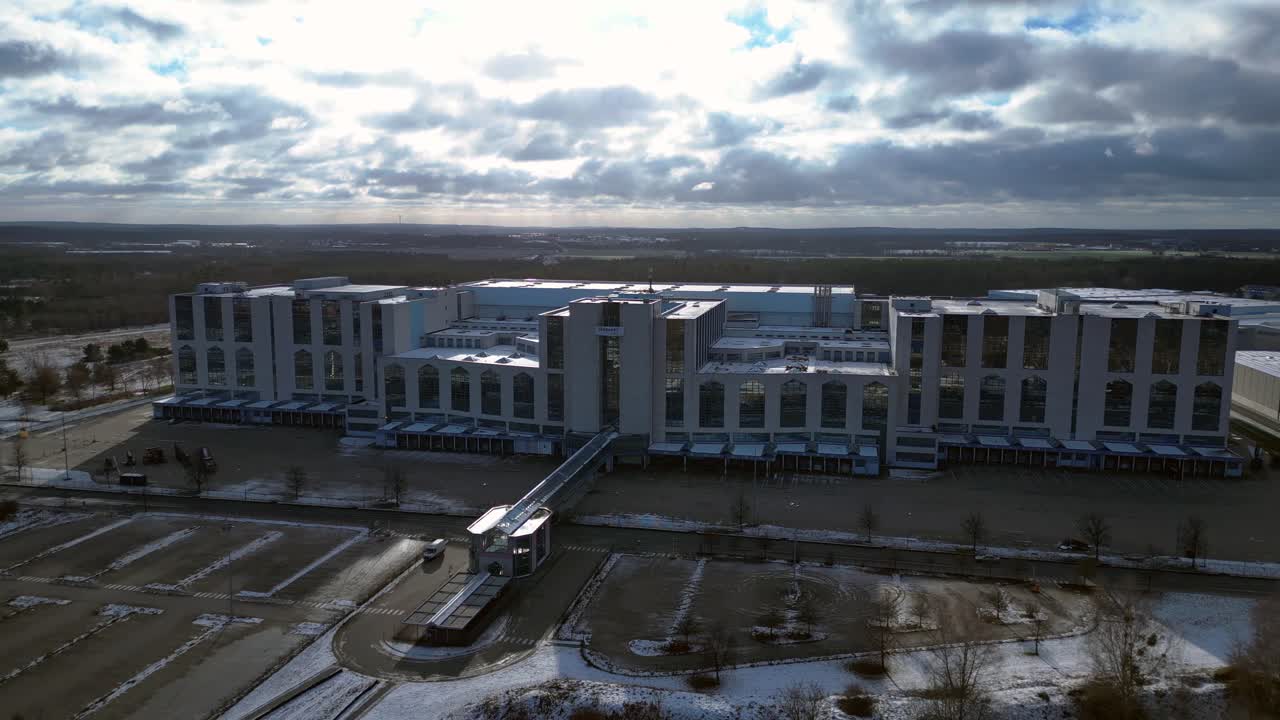 Large distribution center with loading docks and parking lot under a cloudy sky in winter. Perfect aerial view flight wide orbit overview drone
