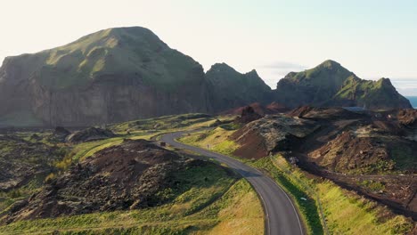 Camino-Sinuoso-A-Través-De-Colinas-Cubiertas-De-Verde-Y-Terreno-Accidentado-De-Las-Islas-Westman,-Con-Un-Cielo-Despejado-Al-Amanecer