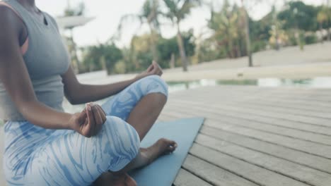 Low-section-of-biracial-woman-practicing-yoga-meditation-sitting-on-jetty,-copy-space,-slow-motion