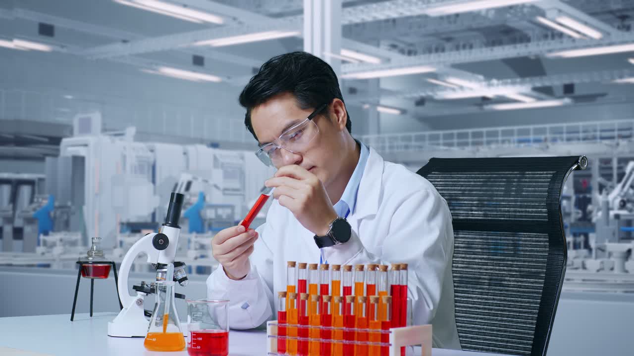 연구실에서 현미경으로 작업하는 동안 실험 튜브에 있는 오렌지색 액체를 조심스럽게 바라보는 아시아 남성 과학자의 가까운 측면 뷰