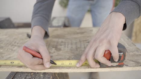 craftsman male hands using tape measure and pen to mark wood