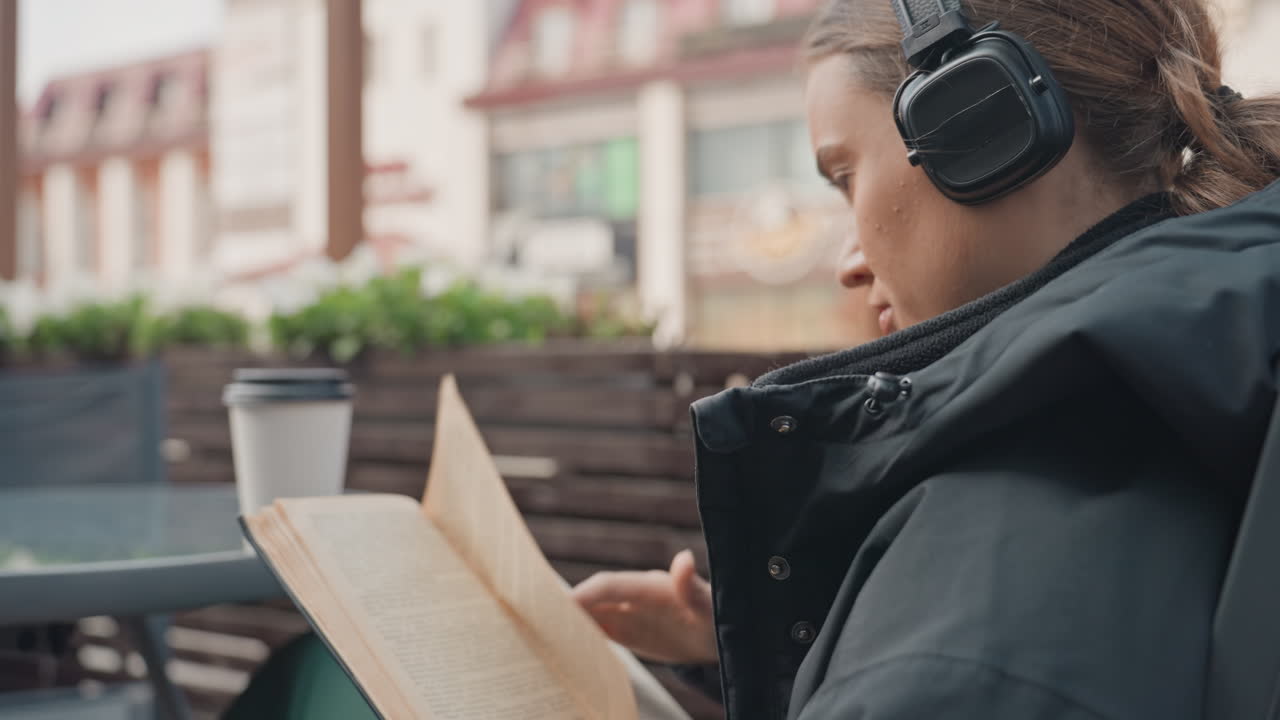 Woman enjoying book in winter clothes, Female reading document peacefully in outdoor winter environment, Young lady listening to music while comfortably reading outside during cold weather