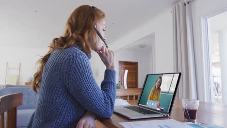 mujer caucásica usando portátil y auriculares de teléfono en videollamada con una colega