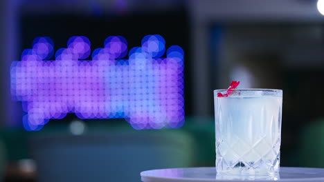 old-fashioned glass with drink on the rotating table. cocktail decorated with red flower in the bar. close up. blurred backdrop.