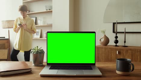 mujer usando teléfono, portátil con pantalla verde en una oficina en casa