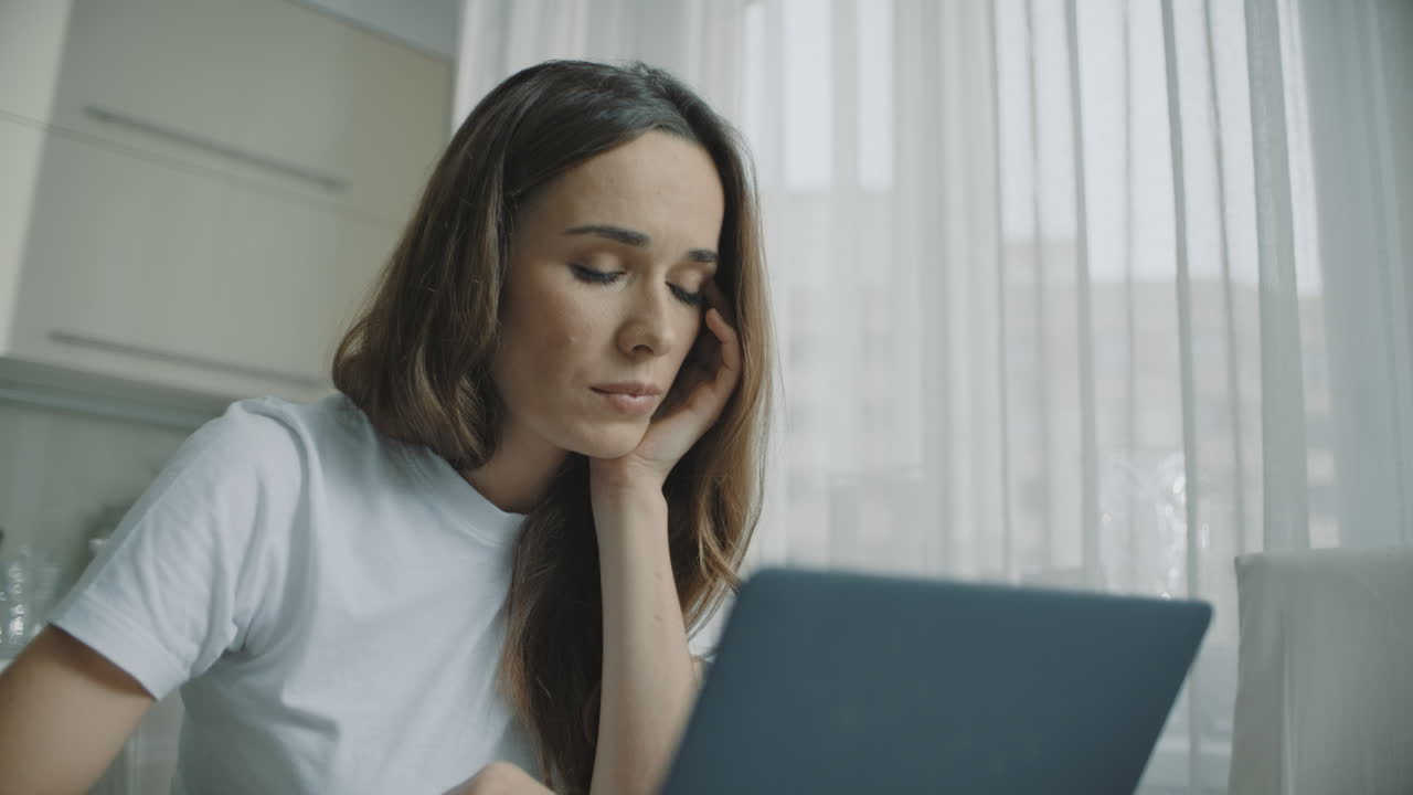 Tired woman working on laptop computer at home