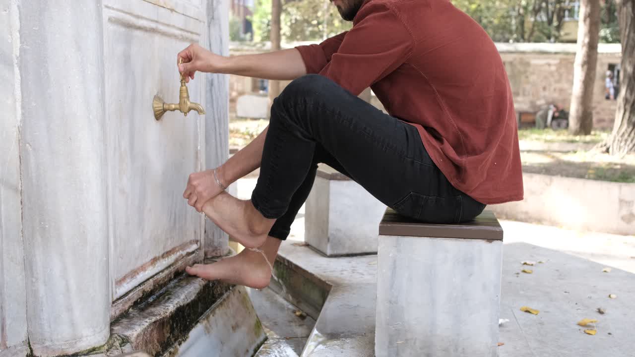 Portrait of caucasian man muslim perform ablution at the mosque, young man washing his feet in the fountain