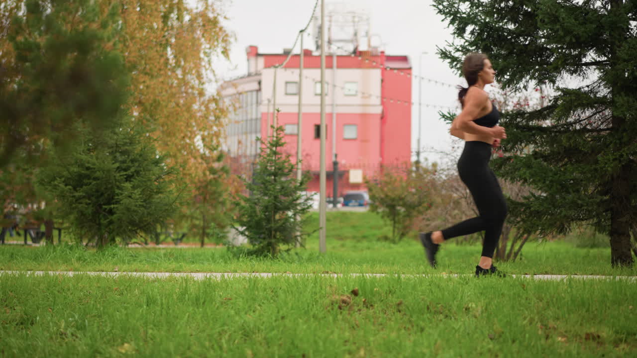 Lady in black top and leggings jogged past vibrant green trees and a building in the background, showing healthy lifestyle and fitness through a peaceful urban park