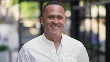 y un hombre adulto con paja en una camisa blanca está de pie en un café sonriendo y posando para la cámara