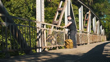 young man traveler with backpack admiring the nature from a rusty old bridge outdoors on sunny summer day