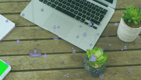 animación de una red de iconos digitales contra un primer plano de equipos de oficina en una mesa de madera