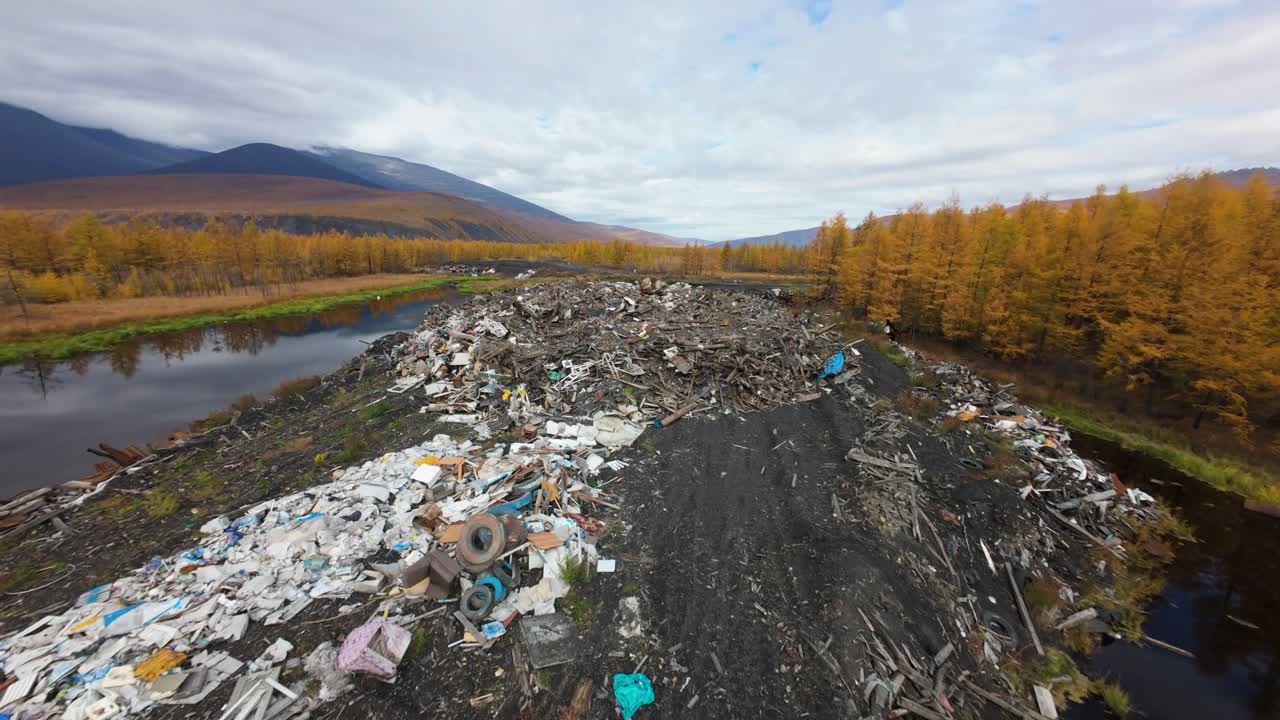 A large heap of household waste dominates the landscape, surrounded by golden autumn trees and serene mountains. This striking contrast highlights the environmental impact of waste disposal.