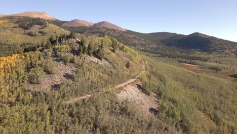 Aerial-view-along-a-remote-mountain-ridge-along-a-dirt-road-with-mountain-peaks-in-the-distance