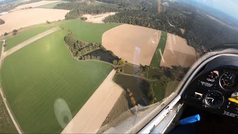 el punto de vista del piloto desde la cabina de un planeador que vuela sobre estanques, campos y bosques.