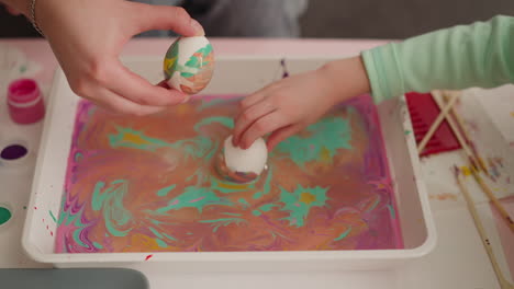 woman and girl roll eggs in oily water with ebru decor mix