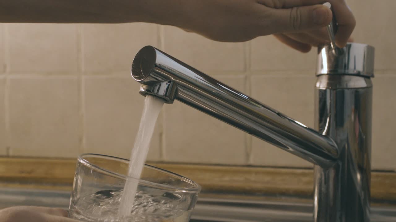 dos manos abren el agua del grifo del fregadero de la cocina y llenan un vaso con agua