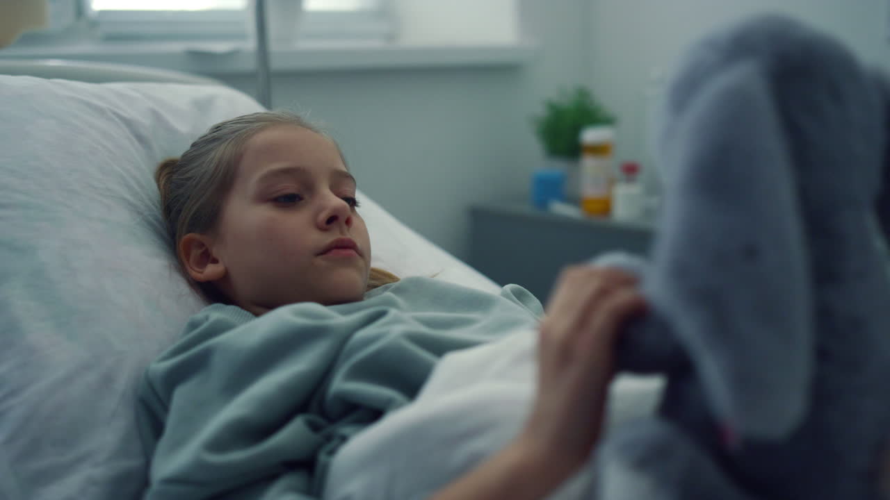 Upset girl lying hospital bed portrait. Sad kid playing with plush toy alone.